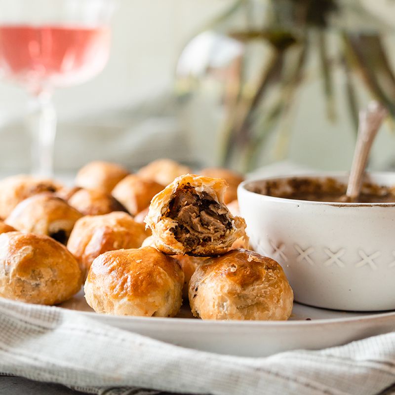Vegan Wellington bites with golden puff pastry served with dipping sauce on a platter.