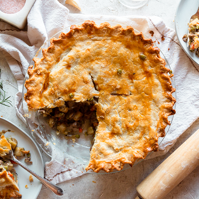 Vegan pot pie with a flaky golden crust and a slice removed to show the vegetable filling
